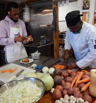 Chefs John Jackson and Rasheen Waters are busy prepping for lunch at The kitchen at Tilda's Kitchen & Market. A bounty of carrots, cabbage, beets, sweet potatoes and butternut squash are from the Farm Hub.